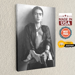 May include: Black and white portrait of Frida Kahlo holding a gun. She is wearing a black blouse, a necklace, and a belt with bullets. The background is a plain wall.