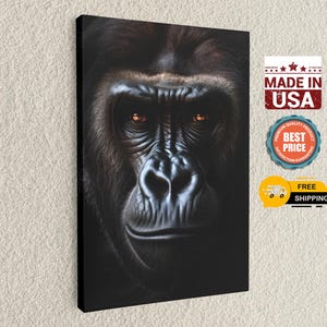 May include: A canvas print featuring a close-up portrait of a gorilla. The gorilla's face is detailed with dark fur, deep wrinkles, and intense orange eyes. The print includes the text "MADE IN USA".