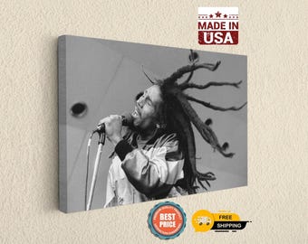 May include: A black and white canvas print featuring a portrait of Bob Marley singing into a microphone with his dreadlocks flowing outward. The image includes a rectangular stamp in the top right corner with the text MADE IN USA.