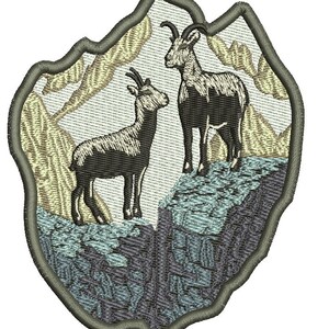 Puede incluir: Parche bordado con dos cabras montesas marrones y negras de pie en un acantilado rocoso con un fondo de montaña beige y azul.