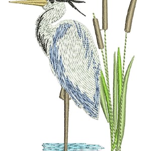 Könnte beinhalten: Gesticktes Design eines Reihers, der im Wasser steht, mit Rohrkolben im Hintergrund. Der Reiher hat weiße, blaue und schwarze Federn, einen langen gelben Schnabel und steht auf einem Bein. Die Rohrkolben sind braun und grün.