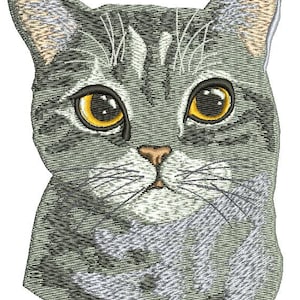 May include: Embroidered image of a cat's face. The cat has gray and white striped fur, large yellow eyes, and a small pink nose. The cat's whiskers are visible, and the image is detailed with various thread colors.