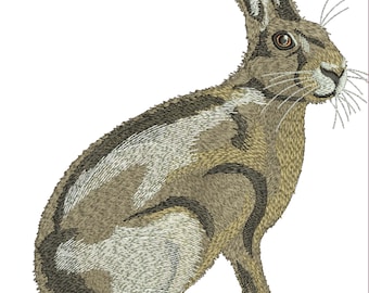 Peut inclure: Image brodée d'un lièvre assis. Le pelage du lièvre est un mélange de marron, de beige et de blanc, avec des coutures détaillées créant de la texture. Le lièvre a de longues oreilles, un visage détaillé et des moustaches. Le fond est blanc uni.
