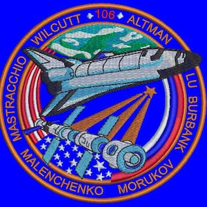 Può includere: Toppa ricamata raffigurante uno space shuttle e una stazione spaziale, con i nomi degli astronauti e il numero 106. La toppa ha uno sfondo blu con un design circolare e un effetto a stella.
