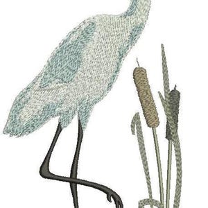 May include: An embroidered design of a white heron standing in water, with cattails in the background. The heron has a long, curved neck, black legs, and a yellow beak. The design is detailed and appears to be a patch or applique.