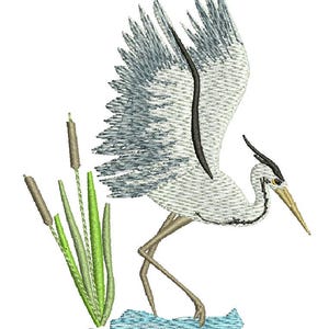 May include: An embroidered design of a heron with outstretched wings, standing in water. The bird is primarily white and gray, with black accents and a yellow beak. Green reeds and cattails are in the foreground, with a light blue water effect.