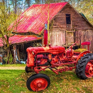 May include: A red vintage tractor parked in front of a red barn with a wooden exterior. The tractor has a large rear tire and a smaller front tire. The barn has a wooden door and a window.