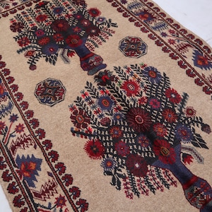 May include: A beige rug with a traditional Persian design featuring two stylized floral arrangements in shades of red, blue, and black. The rug has a border with a repeating pattern of stars and geometric shapes.