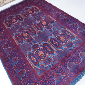 May include: A rectangular, hand-woven rug with a central medallion design. The rug features a deep blue field with intricate patterns in red, blue, and touches of orange. The border is a darker blue with geometric motifs. The rug has a fringed edge.