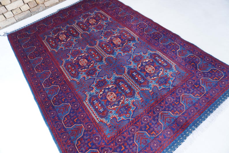 May include: A rectangular, hand-woven rug with a central medallion design. The rug features a deep blue field with intricate patterns in red, blue, and touches of orange. The border is a darker blue with geometric motifs. The rug has a fringed edge.
