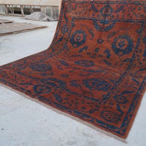 May include: A rectangular area rug featuring a deep orange background with a dark blue floral pattern. The design includes a central medallion and a wide border with intricate botanical motifs. The rug has a short fringe along the bottom edge.