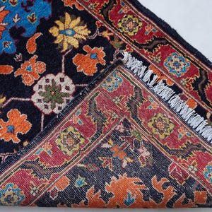 May include: An intricately patterned rug with a dark blue background and a vibrant floral design in shades of orange, yellow, and blue. The rug's border is red with a repeating geometric pattern, and it has a fringed edge.
