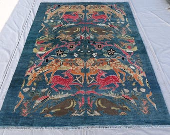 May include: A rectangular teal rug with a detailed pattern of deer and floral motifs in shades of red, orange, and brown. The rug has a fringe along the bottom edge and is displayed on a white surface. This rug is suitable for a living room or bedroom.