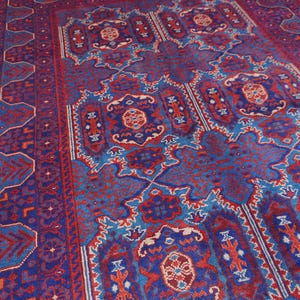 May include: A rectangular, hand-woven rug with a detailed, geometric pattern. The rug features a deep blue background with intricate designs in red, light blue, and cream. The border has a repeating pattern, and the central design is symmetrical.