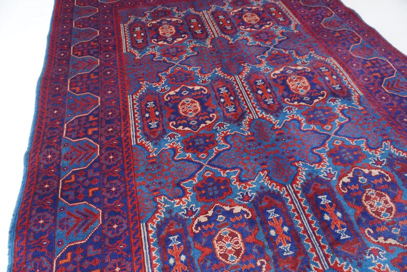 May include: A rectangular, hand-woven rug with a detailed, geometric pattern. The rug features a deep blue background with intricate designs in red, light blue, and cream. The border has a repeating pattern, and the central design is symmetrical.