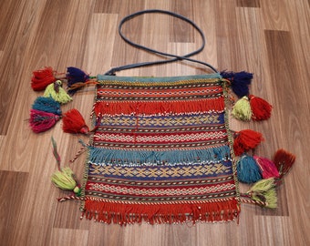 Può includere: Una borsa colorata in tessuto con una tracolla blu e frange. La borsa ha un motivo geometrico in rosso, blu, verde e giallo.