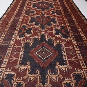 May include: A rectangular rug with a geometric pattern in shades of brown, black, and beige. The rug features a central diamond design and repeating border patterns. The rug is likely made of woven material and is suitable for home decor.