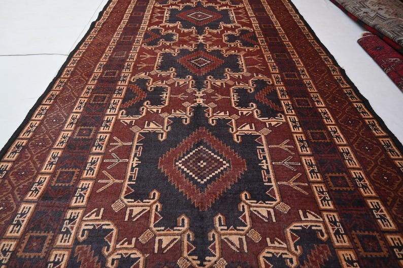 May include: A rectangular rug with a geometric pattern in shades of brown, black, and beige. The rug features a central diamond design and repeating border patterns. The rug is likely made of woven material and is suitable for home decor.