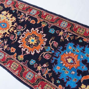 May include: A detailed shot of a dark blue runner rug with a vibrant, intricate floral pattern. The design features orange, yellow, and blue floral motifs, framed by a red border. The rug's design is symmetrical and ornate, suitable for home decor.