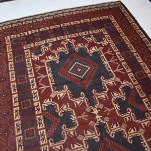 May include: A rectangular, hand-woven rug with a central geometric design in dark blue and burgundy. The rug features intricate patterns and borders in shades of beige, brown, and black. The rug's design is symmetrical and traditional.