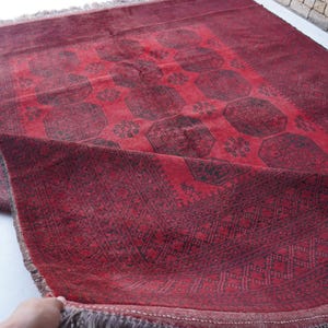 May include: A red and black patterned rug with a geometric design. The rug has a central medallion pattern and a border with intricate details. The rug is made of a woven material and has a fringe on the edges.