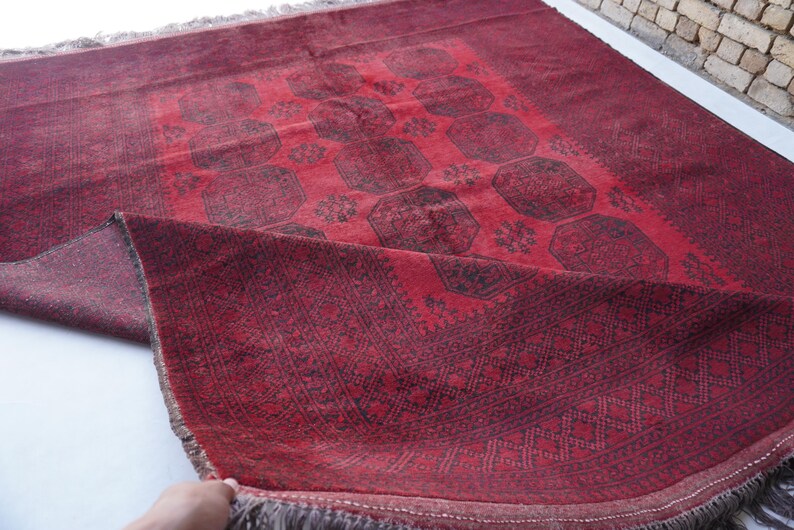 May include: A red and black patterned rug with a geometric design. The rug has a central medallion pattern and a border with intricate details. The rug is made of a woven material and has a fringe on the edges.