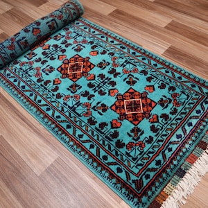 May include: A teal blue rug with a traditional Persian design featuring orange, red, and black accents. The rug has white fringe on the edges.