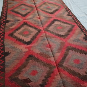 May include: A red, brown, and gray patterned rug with a geometric diamond design. The rug has a fringed edge.