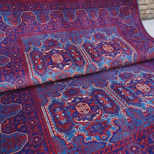 May include: A rolled-up, rectangular rug with a detailed, ornate pattern. The rug features a deep blue background with red and light blue accents. The design includes geometric shapes and floral motifs, creating a traditional aesthetic.