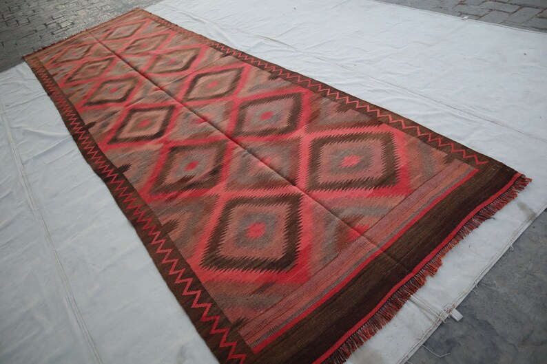 May include: A long, rectangular rug with a geometric pattern of diamonds in shades of red, brown, and gray. The rug has a fringe border.