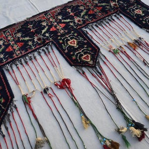 Puede incluir: Textil azul oscuro con dise&ntilde;os florales y en forma de coraz&oacute;n en rojo, blanco y verde. El textil tiene m&uacute;ltiples borlas colgantes en varios colores, incluyendo rojo, beige y negro. Las borlas est&aacute;n adornadas con peque&ntilde;as cuentas.