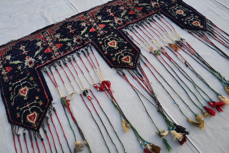 Puede incluir: Textil azul oscuro con dise&ntilde;os florales y en forma de coraz&oacute;n en rojo, blanco y verde. El textil tiene m&uacute;ltiples borlas colgantes en varios colores, incluyendo rojo, beige y negro. Las borlas est&aacute;n adornadas con peque&ntilde;as cuentas.