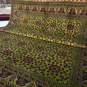 May include: A green and red patterned rug with a geometric design. The rug has a border with a repeating pattern of leaves and flowers.
