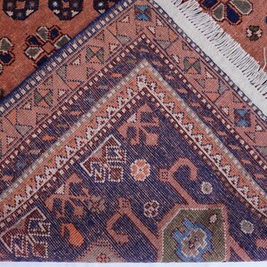 May include: Close-up of a section of a patterned rug. The rug features a complex design with a mix of colors, including shades of red, blue, and beige. The edges of the rug are visible, with a fringe detail.