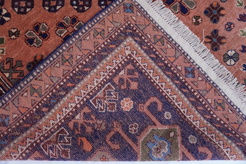 May include: Close-up of a section of a patterned rug. The rug features a complex design with a mix of colors, including shades of red, blue, and beige. The edges of the rug are visible, with a fringe detail.