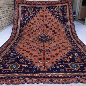 May include: A large, rectangular rug with a detailed geometric pattern. The rug features a central field of coral color, framed by a navy blue border and accents. The design includes floral and geometric motifs.