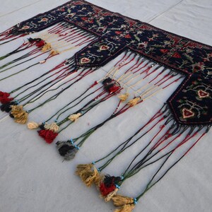 K&ouml;nnte beinhalten: Dunkelblaues Textil mit aufwendigen Blumenmustern und dekorativen Quasten. Die R&auml;nder weisen ein detailliertes Design mit roten, gr&uuml;nen und wei&szlig;en Akzenten auf. Die Quasten sind in verschiedenen Farben gehalten, darunter Gold, Rot und Schwarz.