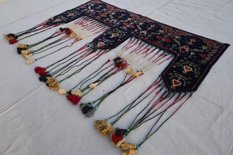 K&ouml;nnte beinhalten: Dunkelblaues Textil mit aufwendigen Blumenmustern und dekorativen Quasten. Die R&auml;nder weisen ein detailliertes Design mit roten, gr&uuml;nen und wei&szlig;en Akzenten auf. Die Quasten sind in verschiedenen Farben gehalten, darunter Gold, Rot und Schwarz.