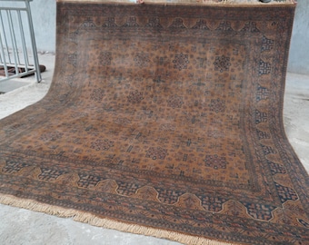 May include: A large rectangular area rug featuring a deep brown field with a repeating pattern of dark blue and black geometric floral motifs. The rug includes a wide border with intricate dark blue designs and light beige fringe at the ends.
