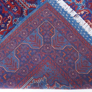 May include: A section of a blue and red patterned rug with a geometric design. The rug has a detailed pattern with a central medallion and a border. The rug's fringe is white.
