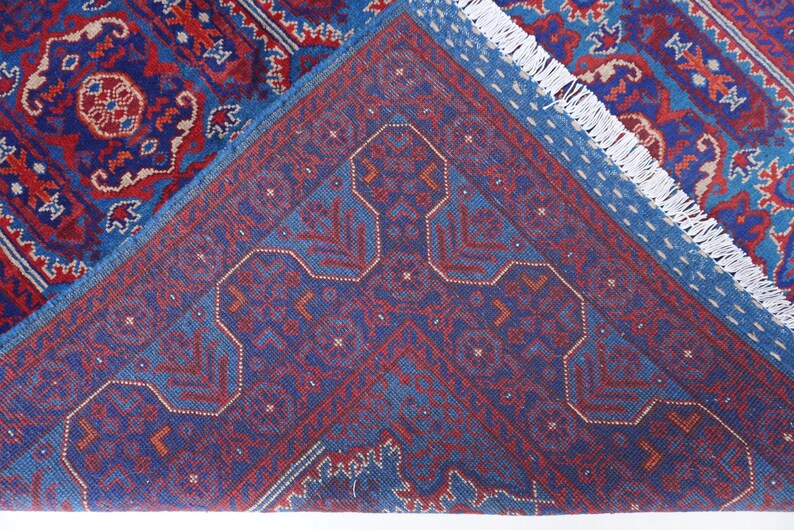 May include: A section of a blue and red patterned rug with a geometric design. The rug has a detailed pattern with a central medallion and a border. The rug's fringe is white.