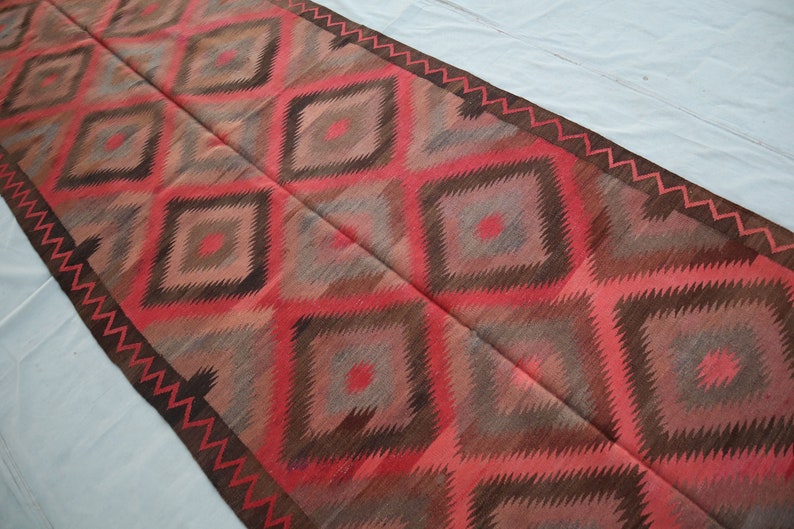 May include: A long, narrow rug with a geometric pattern in shades of red, brown, and gray. The rug has a diamond pattern with a zig-zag border.