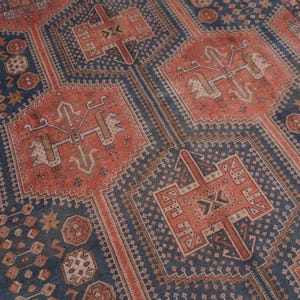 Pu&ograve; includere: Un tappeto antico con un motivo geometrico dettagliato. Il tappeto presenta una combinazione di disegni blu navy e color ruggine, con motivi e bordi intricati. L'estetica generale &egrave; vintage e tradizionale.