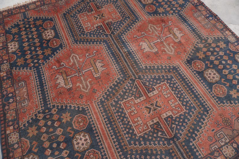 Pu&ograve; includere: Un tappeto antico con un motivo geometrico dettagliato. Il tappeto presenta una combinazione di disegni blu navy e color ruggine, con motivi e bordi intricati. L'estetica generale &egrave; vintage e tradizionale.