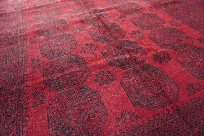 May include: A red rug with a repeating geometric pattern in black. The rug has a central field of red with large octagonal shapes and smaller floral motifs. The border is a darker shade of red with intricate designs.
