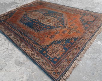 May include: A rectangular area rug featuring a central dark blue diamond medallion surrounded by a burnt orange field. The rug displays intricate geometric and floral patterns throughout, finished with a decorative border and short fringe on the ends.