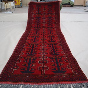 Puede incluir: Una alfombra de pasillo roja con un diseño persa tradicional que presenta árboles estilizados y motivos florales. La alfombra tiene un borde azul oscuro y flecos.