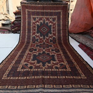 May include: A rectangular, patterned rug with a central geometric design in shades of brown, black, and beige. The rug features intricate borders and a symmetrical pattern, suitable for home decor. The rug is displayed outdoors.
