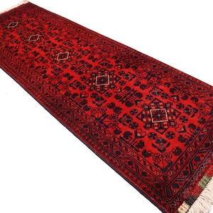 May include: A red runner rug with a traditional Persian design featuring intricate floral and geometric patterns in black and cream. The rug has a fringe border.