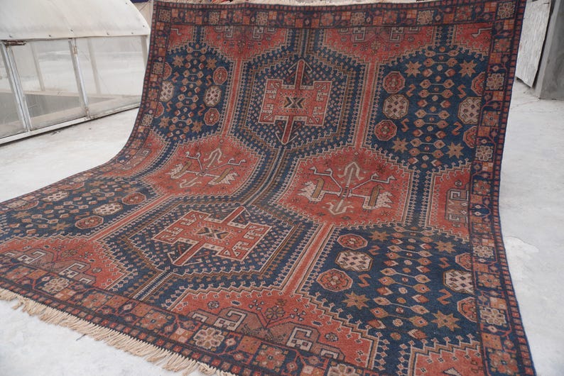Pu&ograve; includere: Un grande tappeto rettangolare con un motivo geometrico nei toni blu navy, ruggine e beige. Il tappeto presenta un motivo a medaglione centrale e dettagli di bordo intricati. Il tappeto ha un bordo sfrangiato.